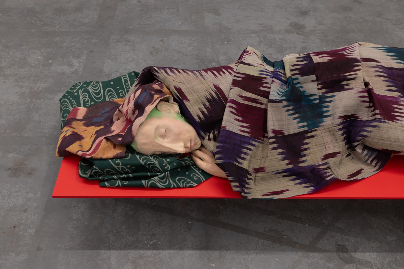 André Romão, The long night, 2025. Polichromed clay, painted wood, Kusaki-zome (silk, Japan, showa era), Ikat (silk, Uzbekistan, c. 1900), Ikat (silk, Uzbekistan, c. 1920), Ikat (cotton and silk, Uzbekistan, c. 1940). 50 x 175 x 55 cm. Unique
