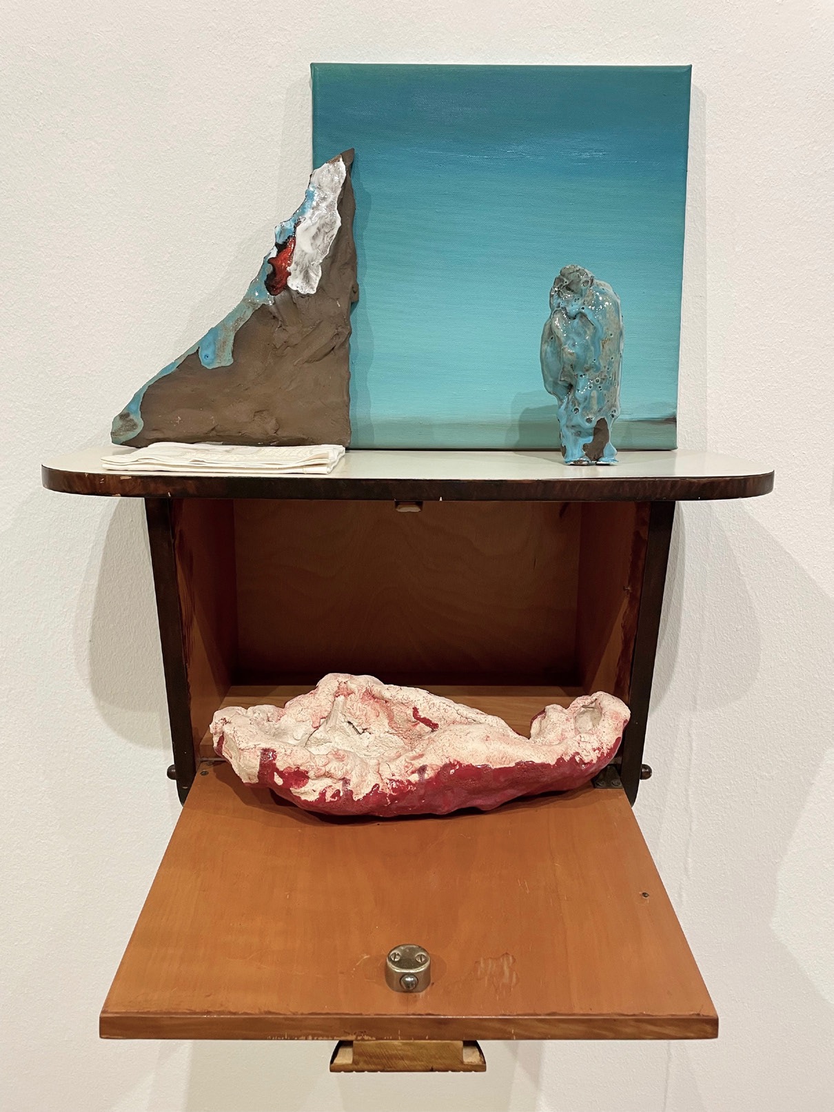 Susanne S. D. Themlitz, Lá, 2022. Ceramic with glaze, oil on canvas, linen napkin with lace, wooden cabinet. 60 x 50 x 38 cm. Unique
