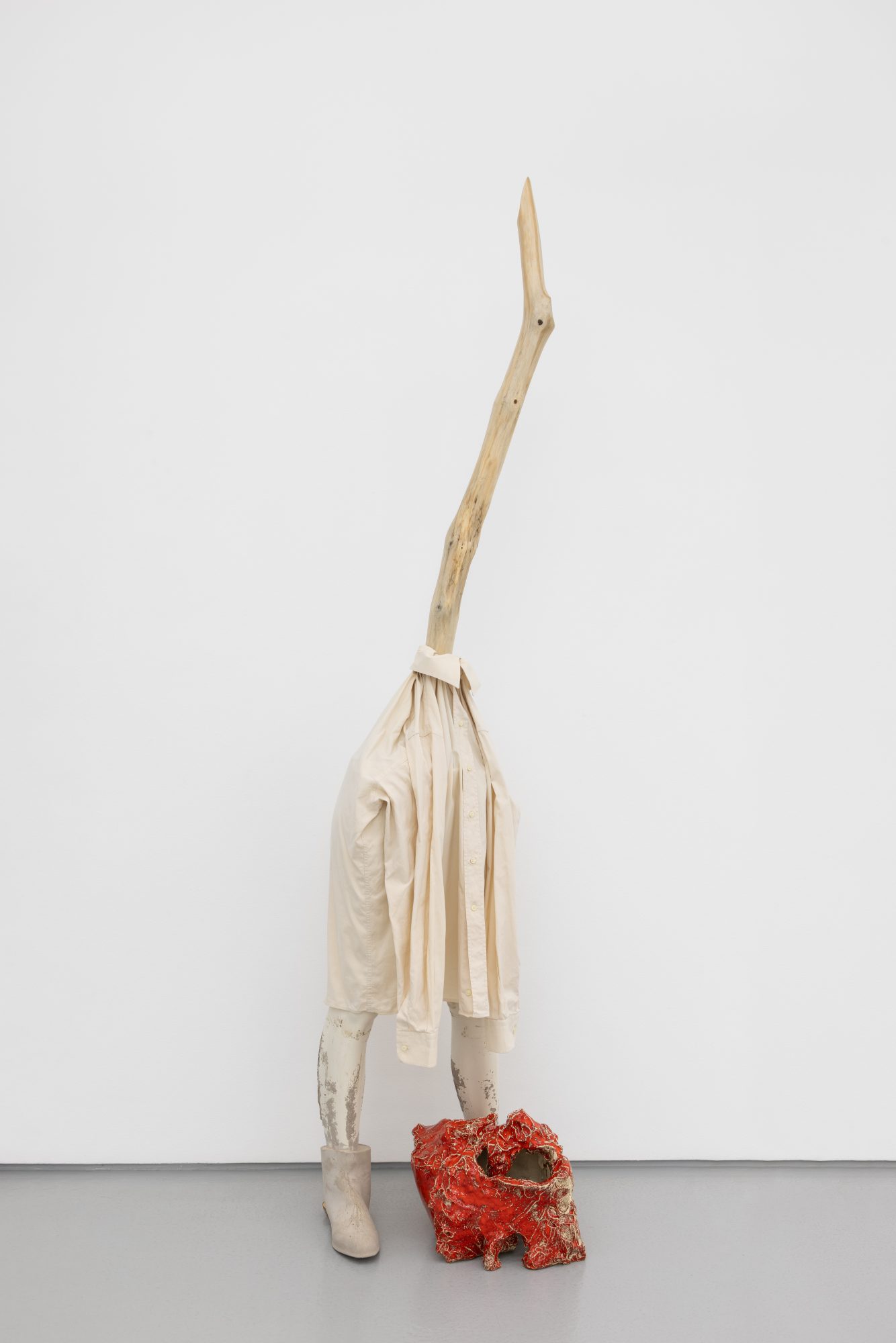 Susanne S. D. Themlitz, The Stretched One/ Comprida, 2025. Wood, cotton shirt, fiberglass, cement, ceramics, elastic, tree branch with lichen. 215 x 48 x 60 cm