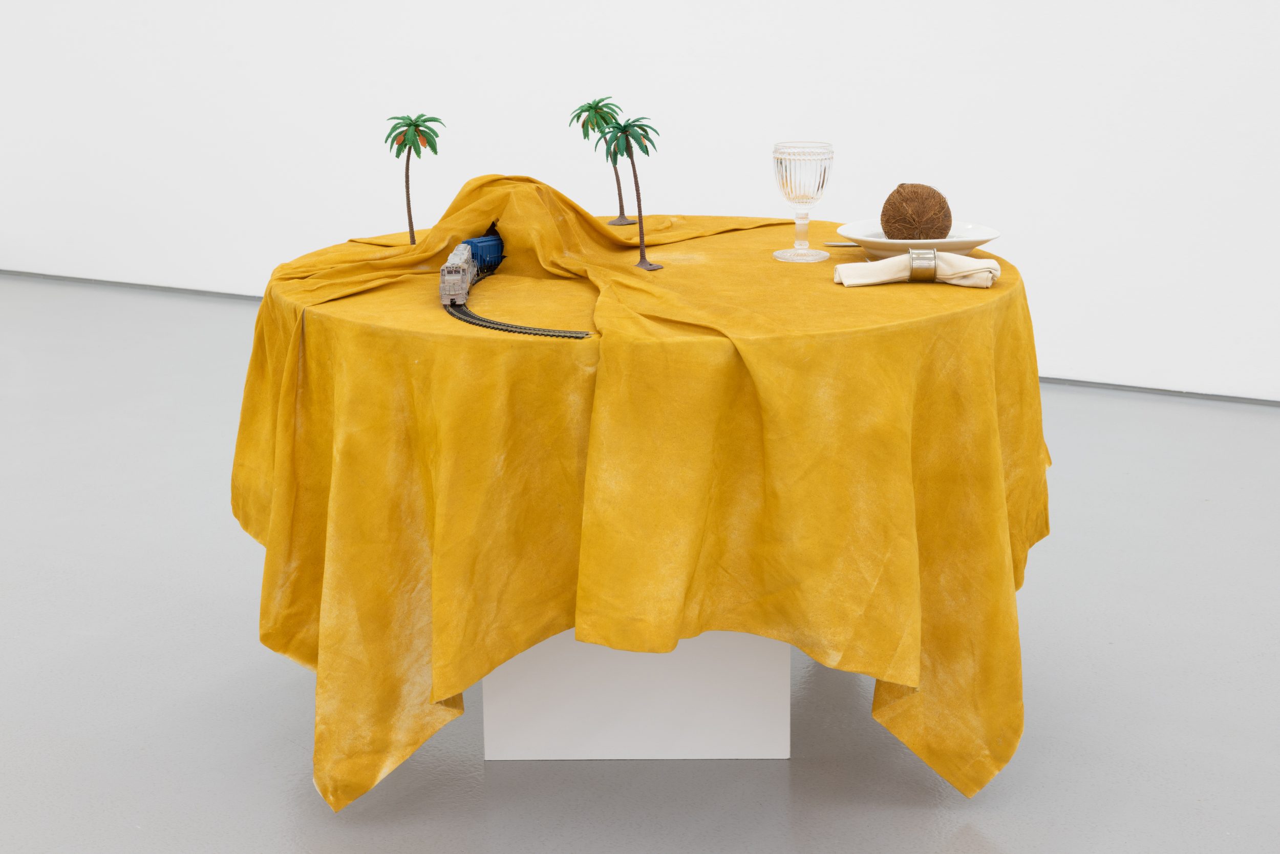 Ana Vieira, Mesa-Paisagem, 1973. Wooden table, fabric, spray paint on fabric, objects (plate, cutlery, napkin ring, napkin, plate, coconut, toy train and plastic palm trees). 94 x Ø110 cm
